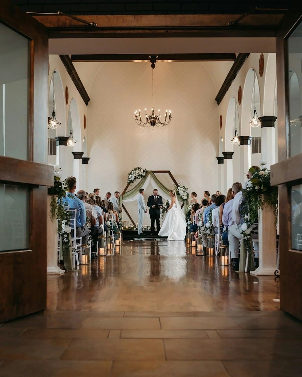 Wedding ceremony in progress in the Grand Room at Hamlet Creek, viewed down the aisle through the entry doors