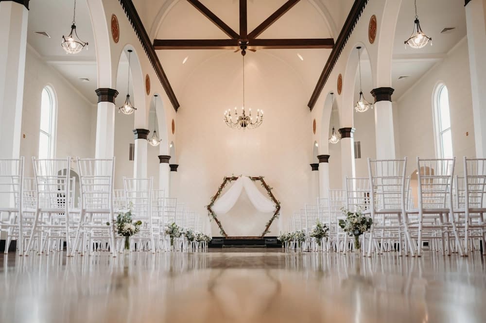 The Grand Room at Hamlet Creek set for a ceremony, with a hexagonal floral arch, chandeliers, and rows of white chairs